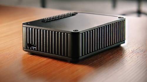 Ad Buster - A Tiny Privacy Powerhouse A sleek black heatsink case housing the Ad Buster device, placed on a modern wooden desk in a well-lit office setting